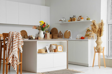 Interior of light kitchen with table, counters and autumn flowers in vase