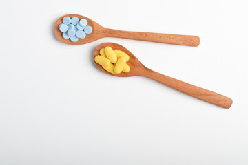 Various vitamin pills and tablets in wooden spoons on white background, top view. Concept of medication, supplement dosage and pharmaceutical products.