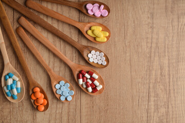 Various vitamin pills and tablets in wooden spoons on wooden table, top view, flat lay. Concept of medication, supplement dosage