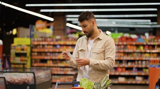 Shocked man checking long grocery receipt at supermarket