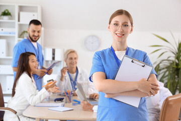 Fototapeta premium Female doctor with clipboard against her colleagues in clinic