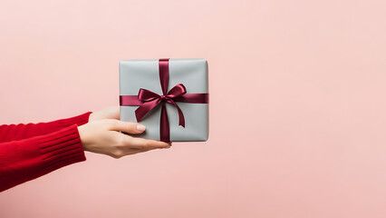 Side View Copy Space on Pink Background Featuring Grey Wrapped Package with Burgundy Ribbon Held by Red Sweater Sleeve