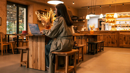 Woman working on laptop in a cozy cafe with warm lighting and wooden decor