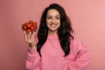 Smiling cute young dark-haired woman posing for the camera on the pink background with her favorite...
