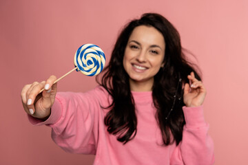 Joyful dark-haired young woman demonstrating her favorite hard candy during the studio photo shoot...