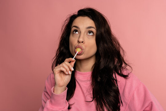 Cute lady licking a yellow lollipop on the plastic stick in front of the camera. Love of sweet food concept