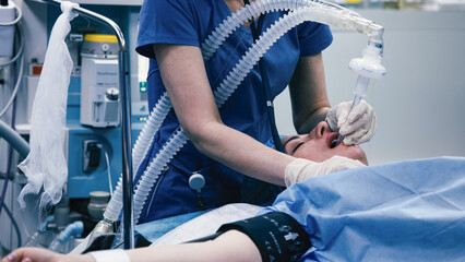 Medical professional in blue scrubs performing anesthesia on patient in operating room, showcasing advanced medical equipment and sterile environment for surgical procedures