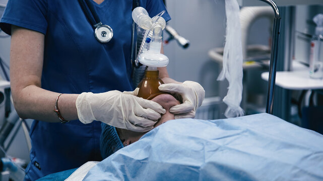 Medical professional in blue scrubs administering anesthesia to a patient in a clinical environment, showcasing critical healthcare procedures and patient care
