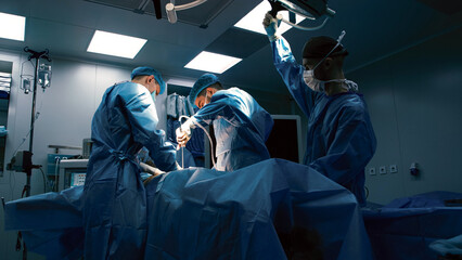 Surgical team of medical professionals in blue scrubs performing a complex operation in a well-lit...