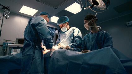 Medical team of surgeons in blue scrubs performing surgery in a sterile operating room, focused on...