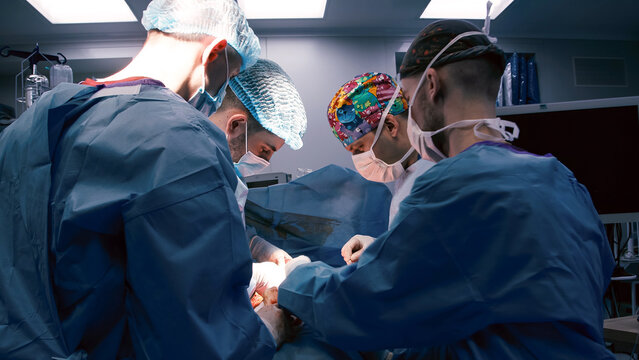 Group of medical professionals, including two surgeons and two assistants, performing a surgical procedure in a modern operating room, showcasing teamwork and precision in healthcare - Powered by Adobe