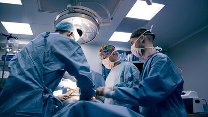 Medical team of diverse surgeons in blue scrubs performing surgery in a bright operating room, showcasing teamwork and precision in a critical healthcare environment
