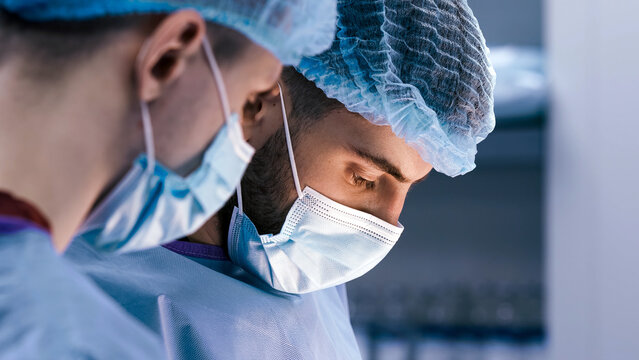 Medical professionals in surgical attire, focused on a procedure, wearing masks and caps, demonstrating teamwork and precision in a clinical environment with advanced medical equipment