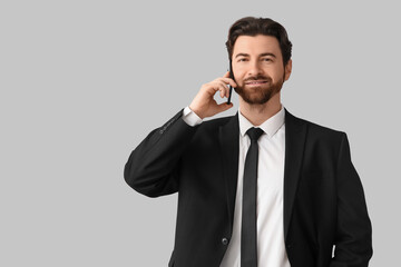 Handsome businessman in stylish black suit talking by mobile phone on light background