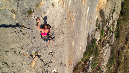 AERIAL TOP DOWN Young female climber pushing up a limestone route in Cikola canyon. Woman searches for a firm handhold to continue lead climbing on natural rock. Adrenaline outdoor activity in Croatia © helivideo