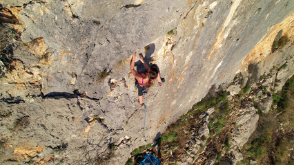 AERIAL TOP DOWN: Agile woman leading a steep limestone route, arms stretched between holds while her blue rope trails below. Adrenaline rock climbing on exposed and rugged walls of Cikola canyon.