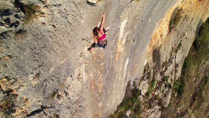 AERIAL: Fearless woman lead climbing high up a challenging limestone wall. Her tiny figure against steep cliff highlights exposure and stunning natural rock texture in famous Croatian climbing area.