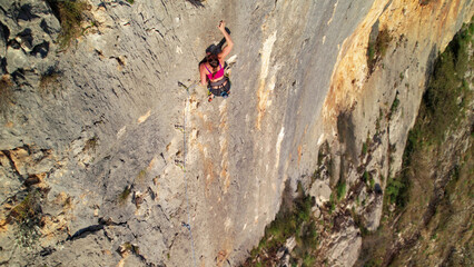 AERIAL: View above a brave female climber high on an exposed limestone face. Young woman lead...