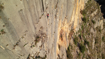 AERIAL: Picturesque limestone wall with a climber climbing a challenging route. Tiny female figure shows skills, technique and agility while dealing with difficult section in an imposing rock face.