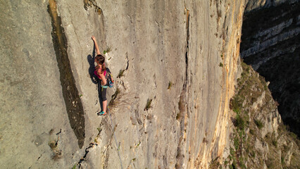 Fototapeta premium AERIAL, CLOSE UP: Young woman moving through a shallow groove on a vertical limestone cliff. Skilled female climber shows precise technique on the exposed and rugged wall above Cikola canyon below.