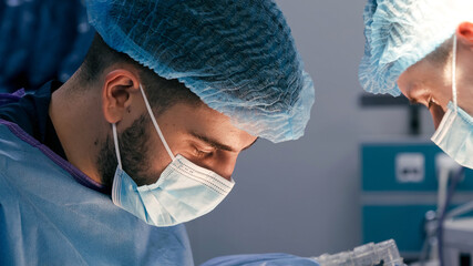 Male surgeon in blue surgical attire focused on patient care, collaborating with another medical professional in a sterile operating room environment
