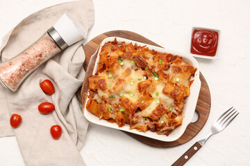 Baking dish with tasty pasta, cut green onion, tomatoes, sea salt and bowl of ketchup on white background