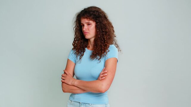 Young woman crossing arms on chest, frowning with offended, angry, upset expression showing negative emotional attitude. Girl on gray background visibly demonstrates dissatisfaction, resentment mood.