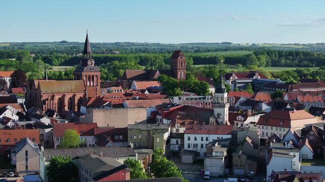 Telephoto aerial view over G&uuml;strow city center, looking toward surrounding hills and Island Lake, showing rooftops and historic urban landscape.