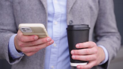 Young man typing on the phone while holding coffee. Slow motion