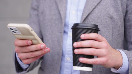 Businessman typing on the smartphone and drinking coffee outdoors. Slow motion