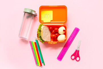 Lunch box with tasty food, bottle of water and school stationery on pink background