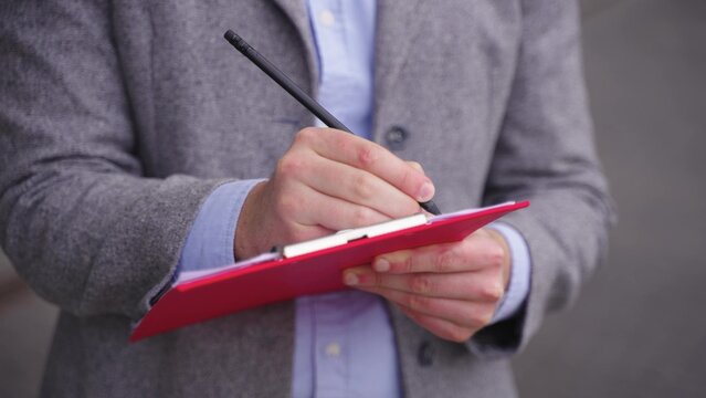 Young man in suit making notes on paper, working outside. Close up. Slow motion