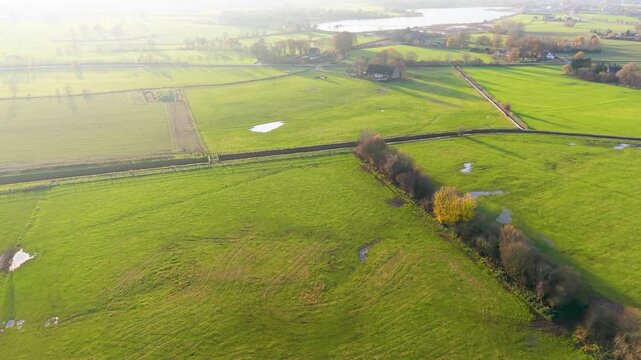Aerial view of rural fields with crop rows, tree shadows, canal, and farm buildings sunlit landscape blending agriculture, infrastructure, and natural geometry.