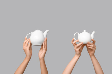 Women with ceramic teapots on grey background