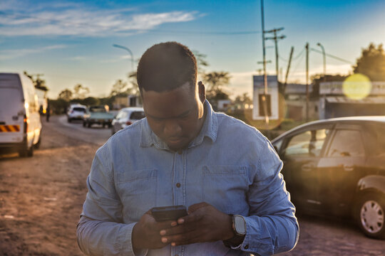 single young african men using a phone in old town at station trading area at sunrise, Johannesburg, South Africa, casual clothing