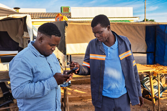 two young african men using a phone in old town at station trading area at sunrise, Johannesburg, South Africa, casual  and workwear clothing