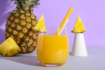 Glass of sweet pineapple juice with fruits slices on table near lilac wall