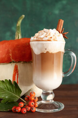 Glass cup of tasty pumpkin latte with cinnamon and star anise on wooden table