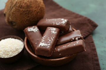 Bowl with tasty chocolate covered coconut candies on green background