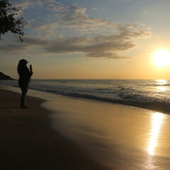 A woman captures a golden sunset on a tropical beach. Perfect for travel, vacation, and relaxation concepts. Ocean waves and sky