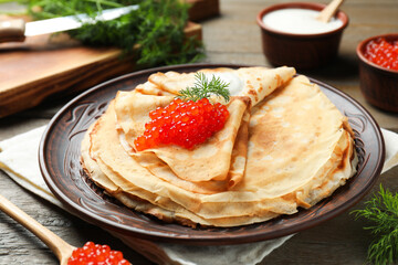 Tasty crepes with red caviar, sour cream and dill on wooden table, closeup