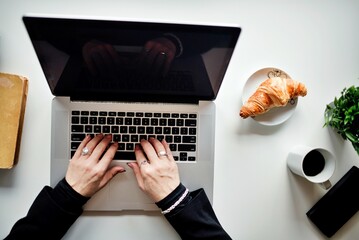 Woman typing on silver laptop over white desk