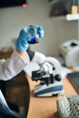 Scientist examining colored liquid in small glass beaker