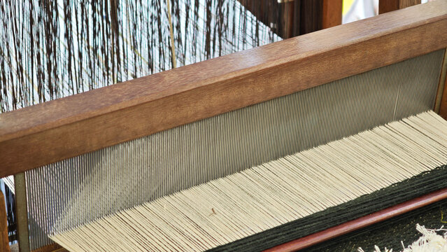 Detailed view of threads stretched across a loom, ready for the weaving process. The focus is on the parallel arrangement of the warp threads, their texture, and the structure of the loom.
