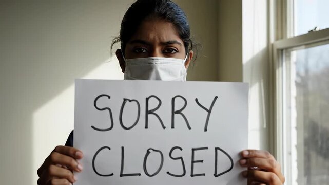 Woman wearing a mask holding a sign saying sorry closed