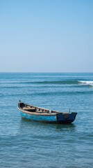 Fototapeta premium Old blue wooden rowboat floating on calm blue ocean water under a clear sky