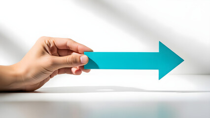 Human hand holding a vibrant turquoise arrow pointing to the right against a bright white background with dramatic side lighting and shadow