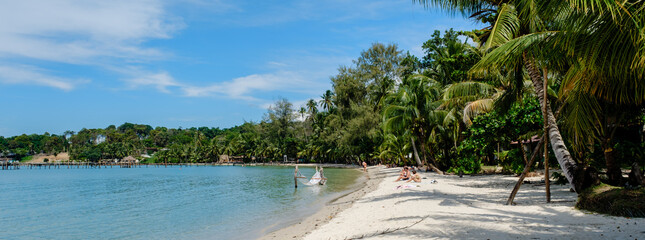 Visitors enjoy a sunny day on the soft sandy beach of Koh Kood Island, surrounded by turquoise waters and tropical trees. TAo Taphao Beach Ko Kut Thailand