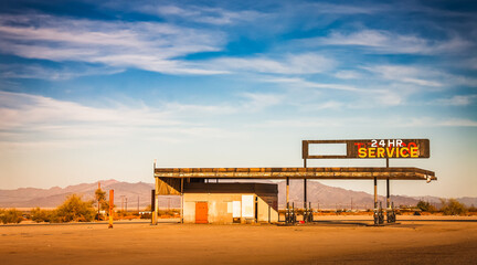 An atmospheric, horizontal photograph of a lonely, abandoned gas station in the California desert, and at night. The vintage "Service" sign suggests a forgotten era of Route 66 travel and road trips. 