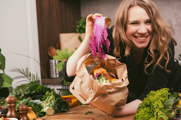 Chef showing cabbage scrap above open paper bag filled with vegetable peels and food waste on kitchen table, demonstrating sustainable cooking process, compost preparation and zero waste routine